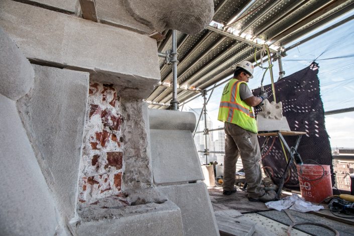 man works on stone while on scaffolding