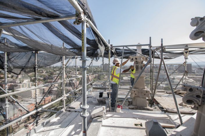 men repair the stone of a church steeple above Denver