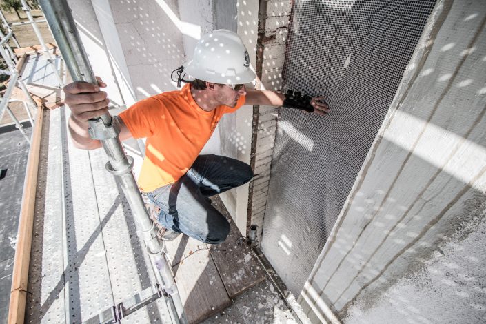 man inspects window covering from scaffolding