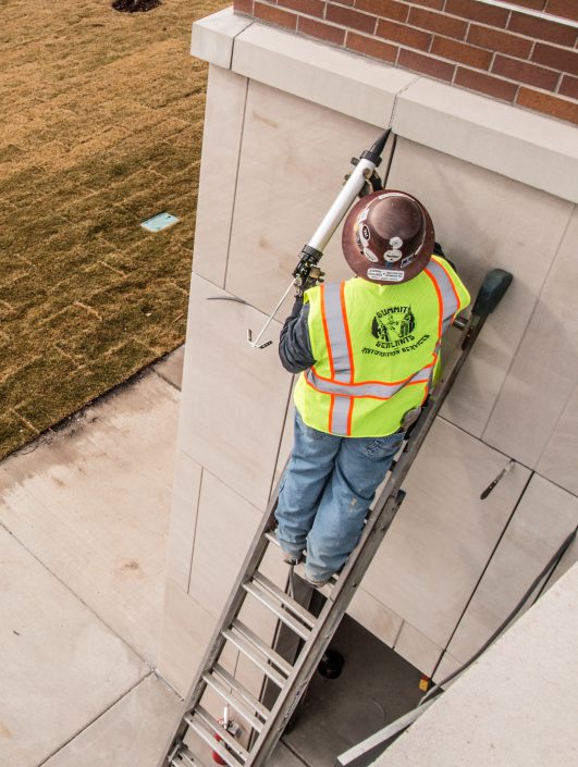 worker on ladder applies caulking to a building exterior