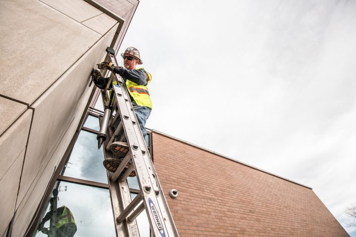 worker on ladder applies backer rod on building exterior