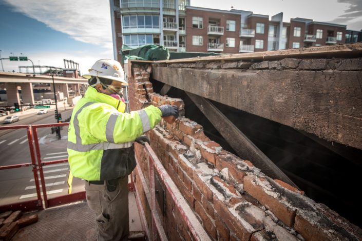 Removing loose bricks during restoration with coors field in the background