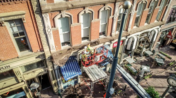 workers install safety netting at Larimer Square from a boom lift