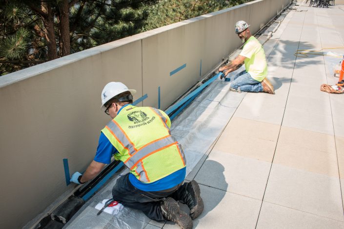 two workers install liquid flashing on a deck