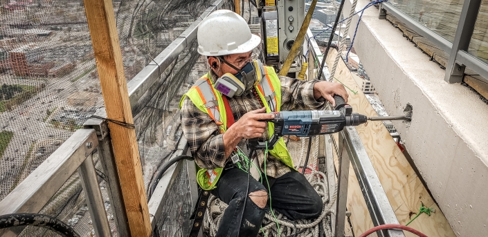 swing stage worker uses a hammer drill