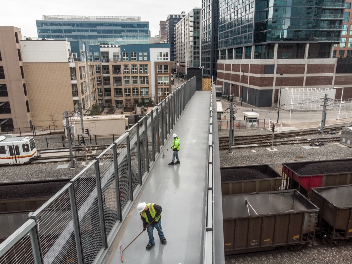 Workers apply a top coat of deck coating to a pedestrian bridge