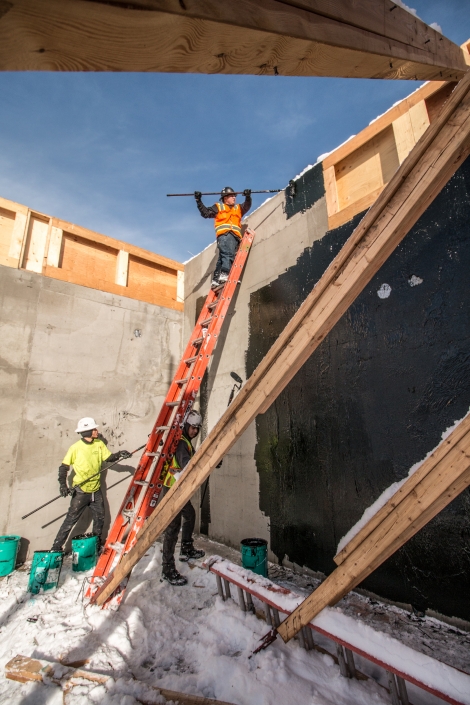 workers apply waterproofing to a foundation