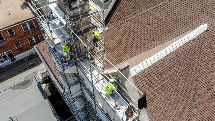 crews perform tuckpointing on a church from scaffolding