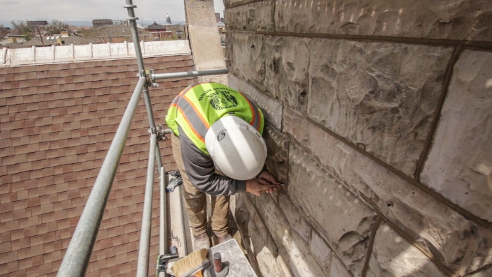 A worker cleans up new mortar on a stone church with scaffolding